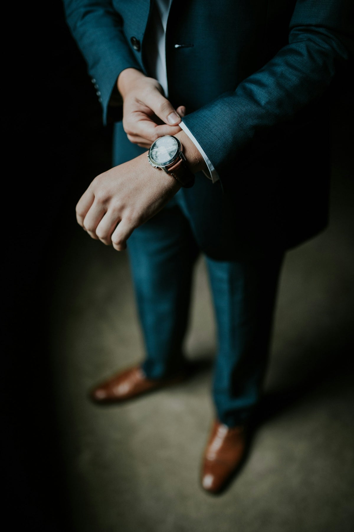 A person in a teal suit adjusting a leather watch on their wrist